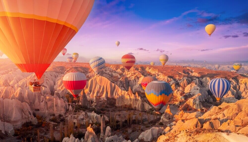 Colorful hot air balloons soaring over the unique rock formations of Cappadocia, Turkey during sunrise Experience magical Turkey tours with JKV Travel.